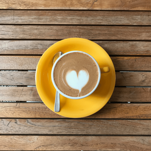 Image of a yellow coffee cup with a love heart coffee art