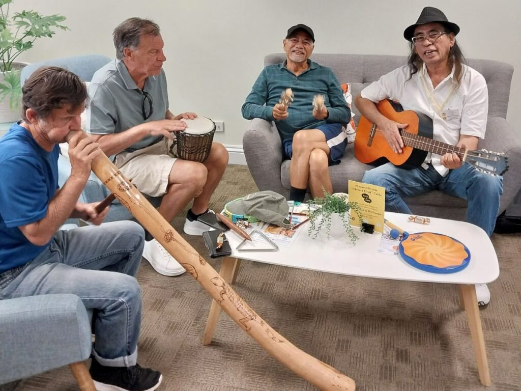 Chatty Cafe volunteer Ron with his guitar surrounded by a group of Chatty Cafe participants playing musical instruments